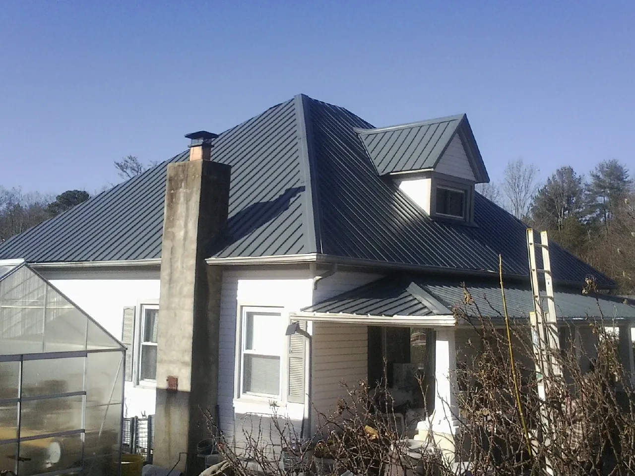 Dark blue standing seam metal roof on a white farmhouse with dormer — Slate & Tile Roof Repair by Roofing Brothers in Harrells