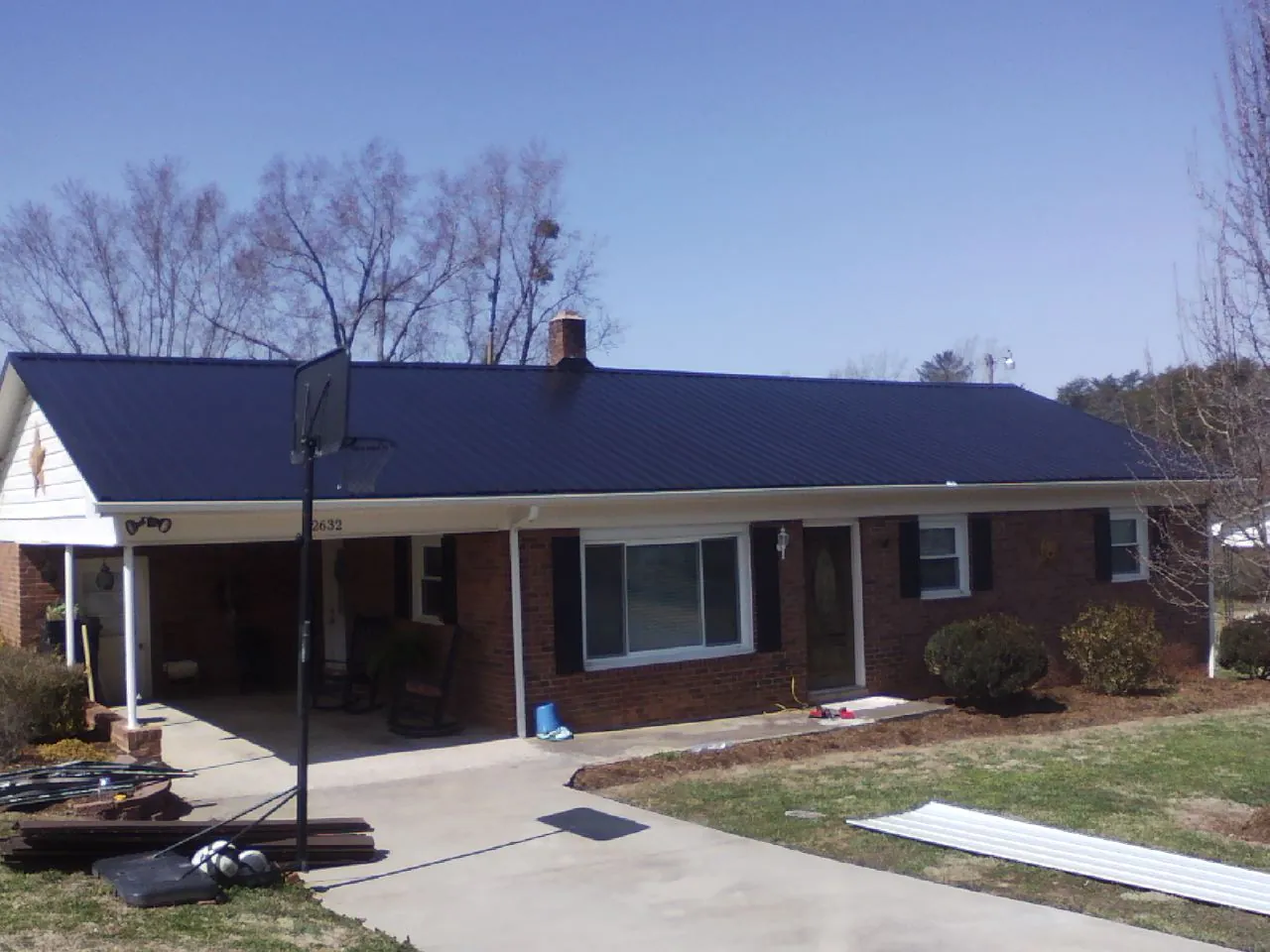 Finished dark blue metal roof on a brick ranch with a carport in Harrells