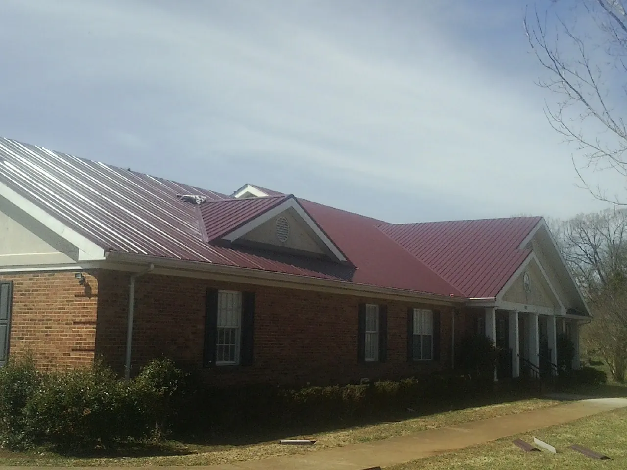Red metal roof with gabled entries on a long brick building, from a Hail Damage Roof Repair job in Harrells