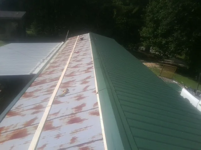 Old rusted panels beside newly installed green metal roofing — Wind Damage Roof Repair by Roofing Brothers in Harrells