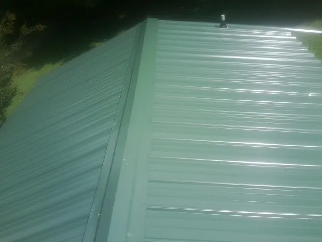 New green metal panels meeting at the ridge of a roof — Flat Roof Repair work by our crew in Harrells