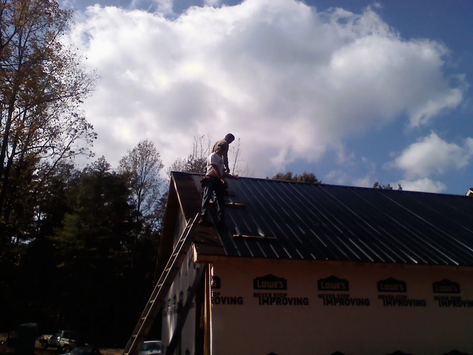 Roofer fastening dark metal panels high against a cloudy sky, from a Roof Inspection job in Harrells