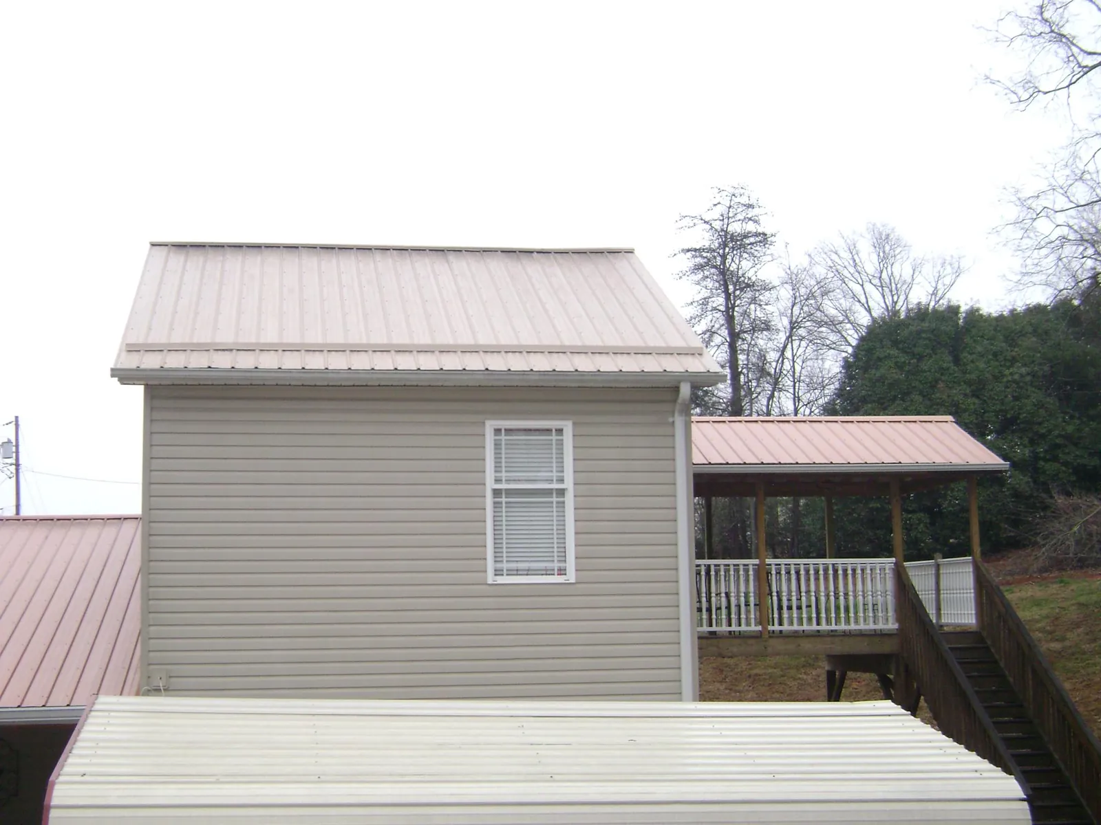 Tan metal roofs on a two story addition and attached porch, from a Roof Replacement job in Harrells